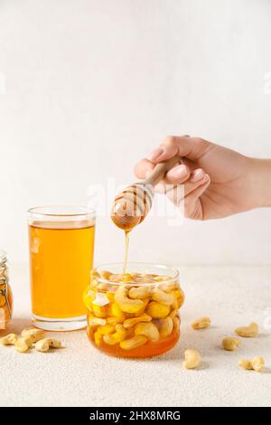 Weibliche Hand mit Dipper und süßen Cashewnüssen in Honig auf hellem Hintergrund Stockfoto