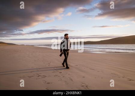 Ein Fotograf, der während des Sonnenuntergangs den Strand von Luskentire auf der Insel Harris erkundet. Stockfoto