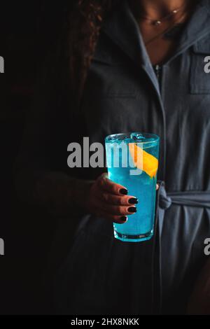 Frau mit blauem Cocktail in einem Highball mit Eis Stockfoto