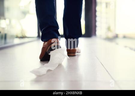 Seine Verlegenheit mit sich schleppen. Nahaufnahme eines Geschäftsmannes, der mit Toilettenpapier an seinem Schuh in ein Büro läuft. Stockfoto