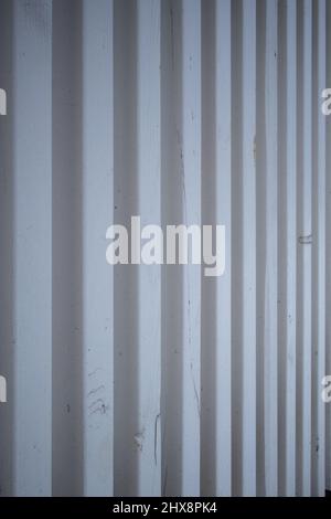 Abstrakter Hintergrund bestehend aus weißen Metallstreifen. Vertikaler Zaun aus Metalllatten. Streifenmuster mit unscharfem Hintergrund. Bemalt und te Stockfoto
