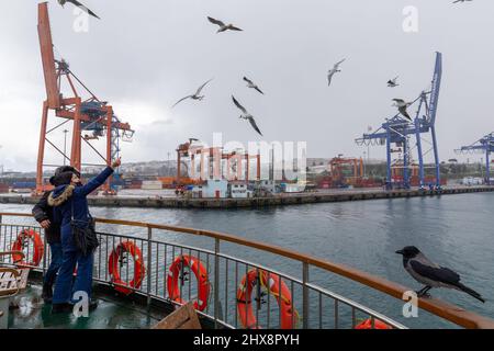 Istanbul, Türkei. 10. März 2022. 10. März 2022: Menschen, die an einem verschneiten Tag Möwen auf der Fähre der City Lines füttern, und der Hafen Haydarpasa im Hintergrund in Istanbul, Türkei, am 10. März 2022. Der Schneefall, der gestern begann und zeitweise andauert, setzt sich in Istanbul fort. Nach den Warnungen der Generaldirektion für Meteorologie verstärkte der Schneefall, der gestern in den hohen Teilen der Stadt begann und in einigen Regionen die ganze Nacht über andauerte, seine Wirkung in den Morgenstunden. Der Schneefall variierte den ganzen Tag über. (Bild: © Tolga Ildun/ZUMA Press Wire) Bild: ZUMA Stockfoto