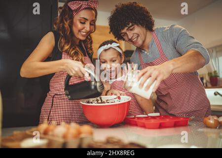 Glückliche Eltern und ihre Tochter sind Cookies gemeinsam in der Küche. Kleines Mädchen hilft, ihre Eltern mischen Teig mit Mixer. Stockfoto