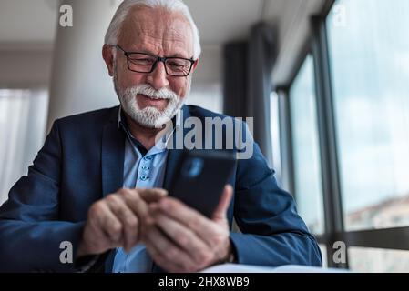 Leitender Geschäftsmann, der mit dem Mobiltelefon nachgeht, in einem modernen Büro Stockfoto
