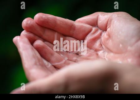 Hand eines dreizehn Jahre alten Jungen, der bei Regen Regentropfen fängt Stockfoto