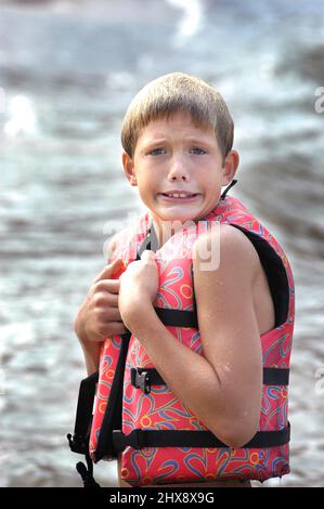 Wet face10 year old Boy in lifeweste PDF in cold of Lake in Fall Stockfoto