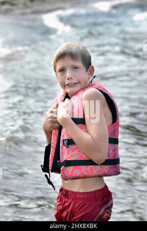 Wet face10 year old Boy in lifeweste PDF in cold of Lake in Fall Stockfoto