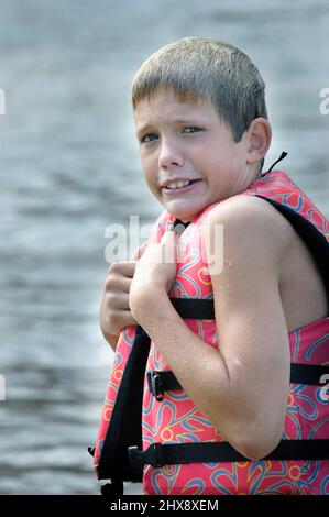 Wet face10 year old Boy in lifeweste PDF in cold of Lake in Fall Stockfoto