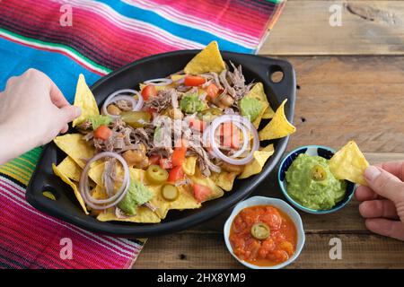 Hände, die Nahrung aus einem Tablett Nachos mit Fleisch nehmen. Schüsseln mit Salsa. Speicherplatz kopieren. Mexikanisches Küchenkonzept. Stockfoto