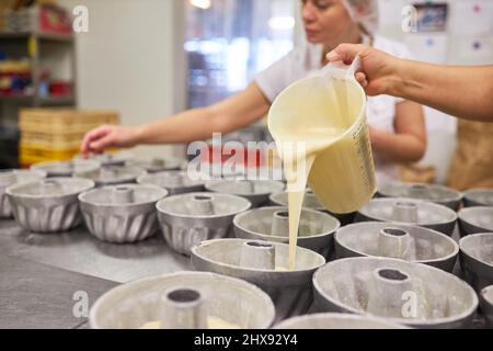 Baker gießt frischen Teig in Gugelhupf-Form während des Backens in der Bäckerei Stockfoto