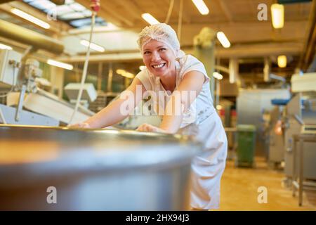 Die junge Frau schiebt als Bäckerlehrling einen Kessel oder einen Kessel für die Produktion in der großen Bäckerei Stockfoto