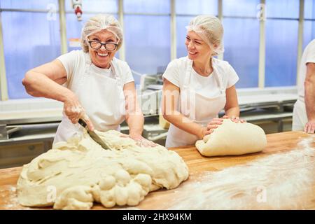 Ältere Frau als Bäckerin mit Erfahrung beim Schneiden und Kneten von Teig in einem Team in der Bäckerei Stockfoto