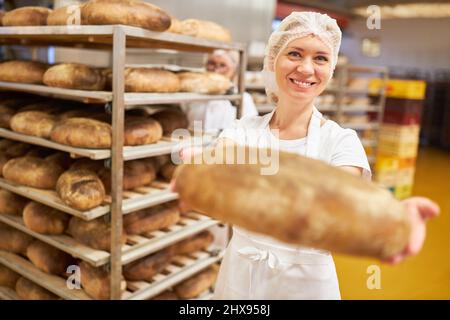 Junge Frau als Bäckerlehrling in der Ausbildung mit gebackenem Brot in der großen Bäckerei Stockfoto