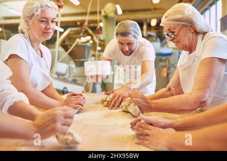 Eine Gruppe von Bäckern mit Auszubildenden kneten den Teig zusammen, um die Brötchen zu backen Stockfoto