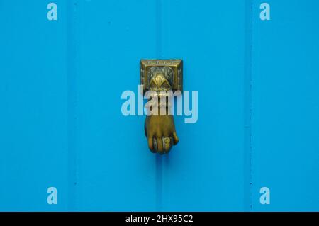 Goldener, eiserner Klopfer mit der Form einer Hand auf einer blauen Holztür. Details Stockfoto