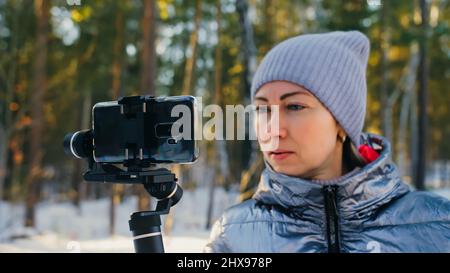 Die professionelle Videografin, die im Winter Smartphone auf einem 3-Achsen-Gimbal-Stabilisiergerät hält. Pro Equipment hilft, qualitativ hochwertige Videos zu erstellen Stockfoto