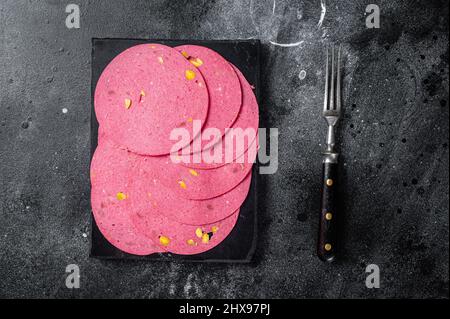 Fleischsalami-Wurstscheiben mit Pistazien-Nüssen auf Marmorplatte. Schwarzer Hintergrund. Draufsicht Stockfoto