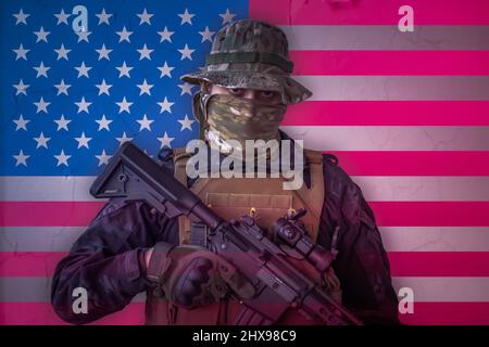 Wütender amerikanischer Soldat, bewaffnet mit Gewehr und US-Flagge als Hintergrund dahinter Stockfoto