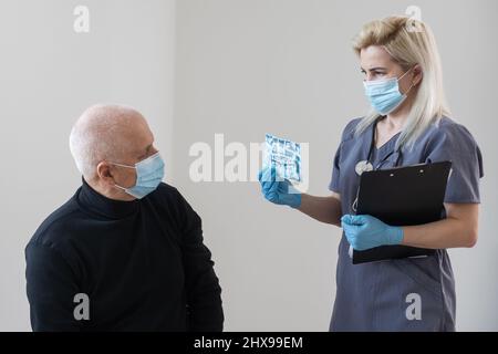 Frau Arzt Zahnarzt arbeitet mit einem älteren Mann in einem Zahnstuhl behandelt Zähne und zeigt Röntgenaufnahmen Stockfoto