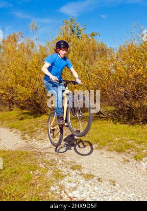 Junge springt mit seinem Dirt Bike über natürliche Rampen im offenen Bereich und genießt Racing Stockfoto