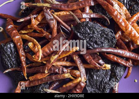 Verschiedene Arten von sonnengetrockneten Paprikaschoten, die zufällig auf einem violetten Hintergrund gestapelt wurden. Lebensmittel und Gemüse. Stockfoto