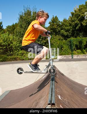 Junge springt mit einem Motorroller über einen Dorn in den Skate Park und genießen es Stockfoto