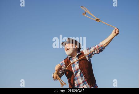 Lasso werfen. Alter Wilder Westen Cowboy mit Seil. Bärtiger Westernmann mit brauner Jacke und Hut, der Pferd oder Kuh fängt. Stockfoto