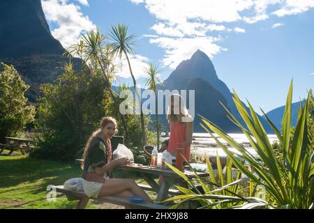 Das Touristenpaar im Milford Sound bietet einen Grilljause und Spaß vor dem berühmten Mitre Peak, zwei Reisende, die im Freien essen und den neuseeländischen Lebensstil pflegen Stockfoto