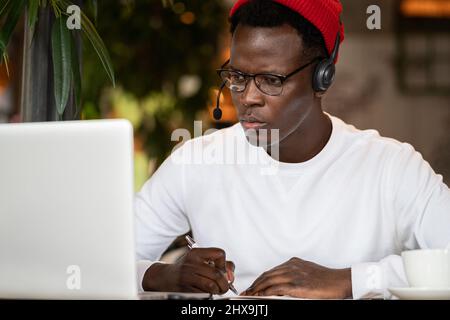 Konzentration schwarzer Hipster männlich in Kopfhörern, Brillen Studing oder Remote am Computer arbeiten Stockfoto
