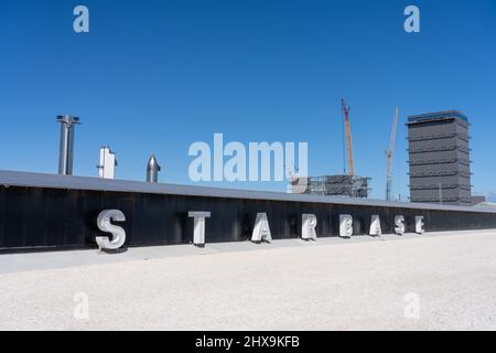 Das Schild an der SpaceX Starbase in Boca Chica in der Nähe von Brownsville, Texas. Dahinter steht ein Raumschiff, eine Super Heavy Booster Rakete und Montagegebäude. Stockfoto