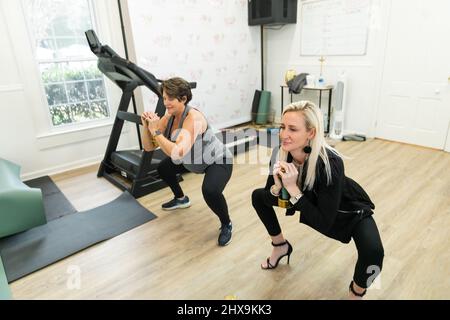 Ein weiblicher Personal Trainer, der einem Klienten hilft, Kniebeugen mit kleinen Handgewichten in einem Gym zu machen Stockfoto