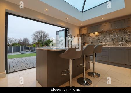 Ultramoderne, hochwertige, graue Küche mit Laterne-Oberlicht und zweiklappbaren Türen Stockfoto