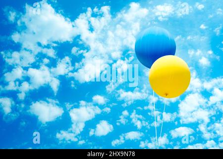 Zwei Luftballons in ukrainischen Flaggen-Farben über blauem Himmel und weißen Wolken. Stockfoto