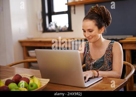 Aktualisieren meines Blogs im alternativen Stil. Aufnahme einer jungen Frau mit Dreadlocks mit einem Laptop zu Hause. Stockfoto