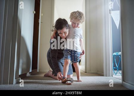 Machen Sie sich bereit für den Spaß vor Ihnen. Aufnahme einer Mutter, die ihrem Sohn hilft, seine Schuhe zu Hause anzuziehen. Stockfoto