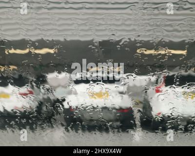 Verschwommene Sicht auf stationäre geparkte Autos durch regenbedeckte Fenster Stockfoto