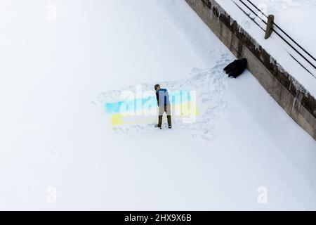 Ein Mann, der auf dem Rideau-Kanal in Ottawa, Kanada, eine gelbe und blaue ukrainische Flagge mit Sprühfarbe auf Schnee malt, um die Ukraine gegen den Krieg zu unterstützen Stockfoto