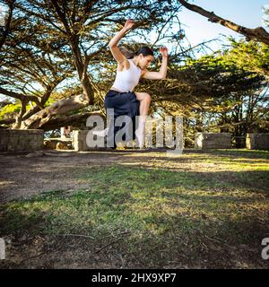 Teenager-Tänzerin beim Springen im baumgesäumten Park Stockfoto