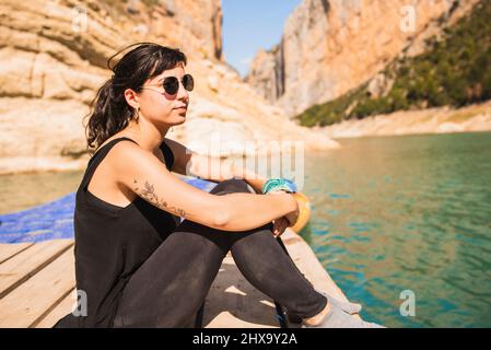 Frau mit Sonnenbrille sitzt auf einem Steg während einer Kajaktour. Stockfoto