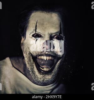 Halloween bringt die Verrückten in dir hervor. Porträt eines bösen Clowns mit Gesichtsfarbe auf schwarzem Hintergrund. Stockfoto