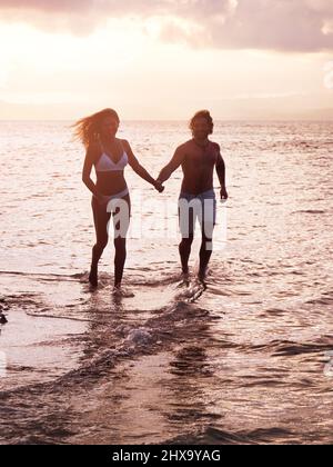 Ihren Urlaub mit vielen lustigen Zeiten füllen. Aufnahme eines jungen Paares, das am Strand entlang läuft. Stockfoto