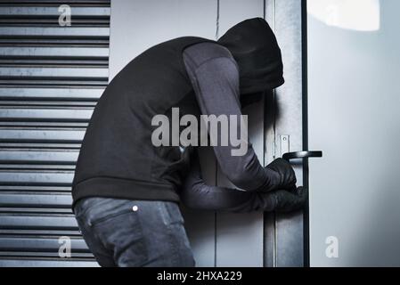 HES hat fast einen Weg gefunden, nach innen zu kommen. Rückansicht eines männlichen Einbrechers, der in einer Garage das Türschloss pflückt. Stockfoto