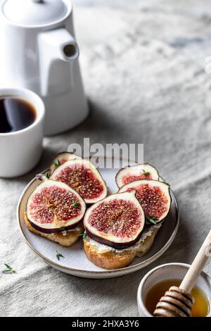 Zwei Sandwiches mit Feigen, Thymian auf strukturiertem Hintergrund. Frühstück Zusammensetzung mit Kaffee, Honig, Leinen Serviette. Vertikale Ausrichtung. Nahaufnahme Stockfoto
