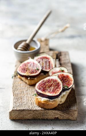 Zwei Sandwiches mit Feigen, Thymian auf einem Holzbrett auf texturiertem Hintergrund Stockfoto