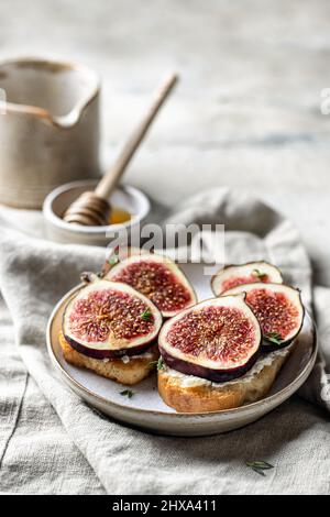 Zwei Sandwiches mit Feigen, Käse, Thymian und Honig mit einem Milchkännchen auf Leinenserviette auf strukturiertem Hintergrund Stockfoto