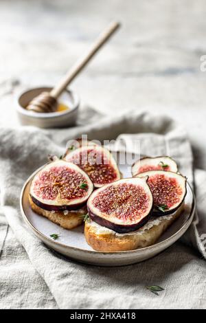 Zwei Sandwiches mit Feigen, Käse, Thymian und Honig auf Leinenserviette auf strukturiertem Hintergrund Stockfoto