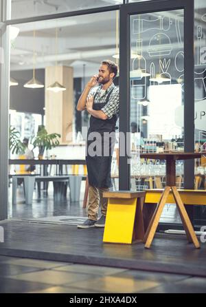 Zufriedene Kunden sind nur einen Anruf entfernt. Aufnahme eines jungen Mannes, der in dem Geschäft, in dem er arbeitet, ein Telefon benutzt. Stockfoto