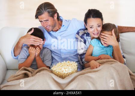 Schauen Sie nicht nach. Zwei Eltern bedeckten die Augen ihrer Kinder, während sie sich einen beängstigenden Film ansahen. Stockfoto