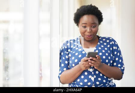 Wow, es muss mein Glückstag sein. Aufnahme einer jungen Geschäftsfrau, die überrascht aussieht, während sie ein Mobiltelefon in einem Büro benutzt. Stockfoto