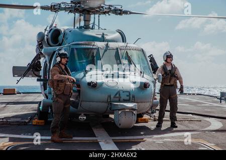 220308-N-GF955-1146 KARIBISCHES MEER - (8. März 2022) -- LT. Kyle „Sunshine“ Suhrie, links, Und Naval Air Crewman (Helicopter) 2. Klasse Dennis Cody, der dem „Shadow Det“ des Helicopter Sea Combat Squadron (HSC) 28, Ablösung 7, zugewiesen wurde, führen während einer Betankungsentwicklung auf dem Flugdeck des Freedom-Variant Littoral Combat Ship USS Billings (LCS 15) am 8. März 2022 Flugkontrollen durch. Billings wird in den Einsatzbereich der US-Flotte für 4. eingesetzt, um die Mission der Joint InterAgency Task Force South zu unterstützen, zu der auch Missionen zur Bekämpfung des illegalen Drogenhandels in der Karibik und im östlichen Pacif gehören Stockfoto